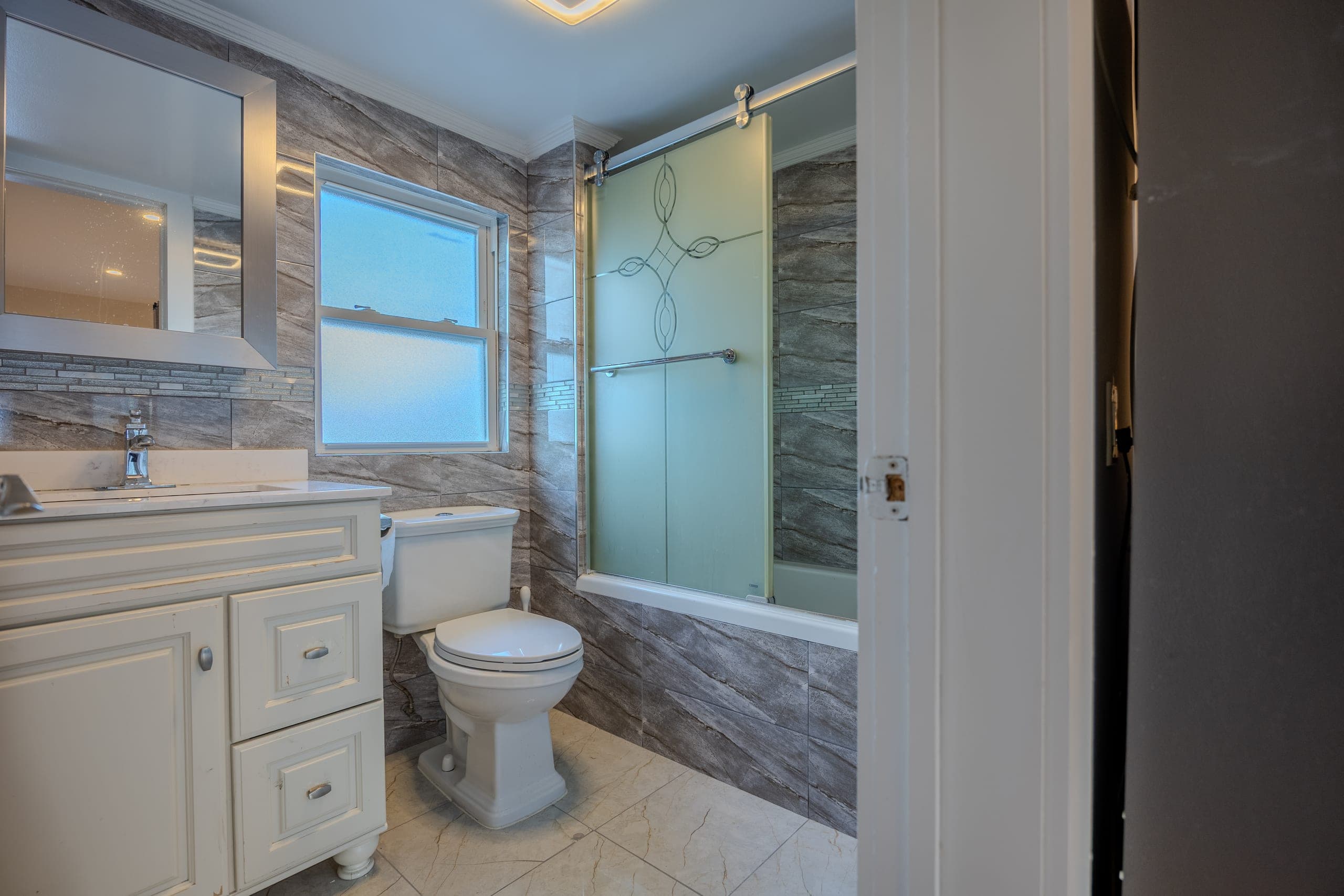 Sayreville, NJ listing photography — remodelled full bathroom with stone-look tile and frosted shower enclosure